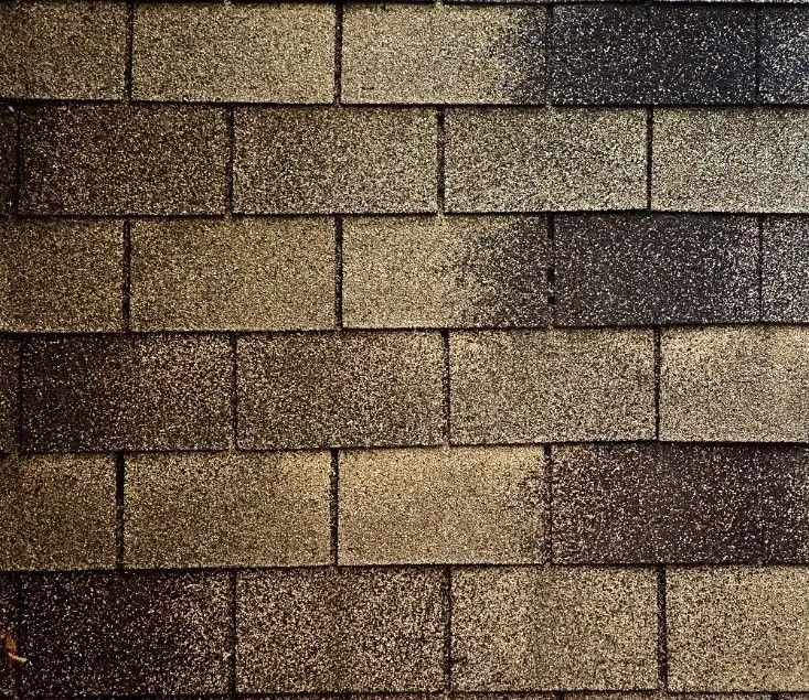 Close-up of weathered asphalt roof shingles with mixed brown and black granules. Close-up of weathered asphalt roof shingles with mixed brown and black granules.