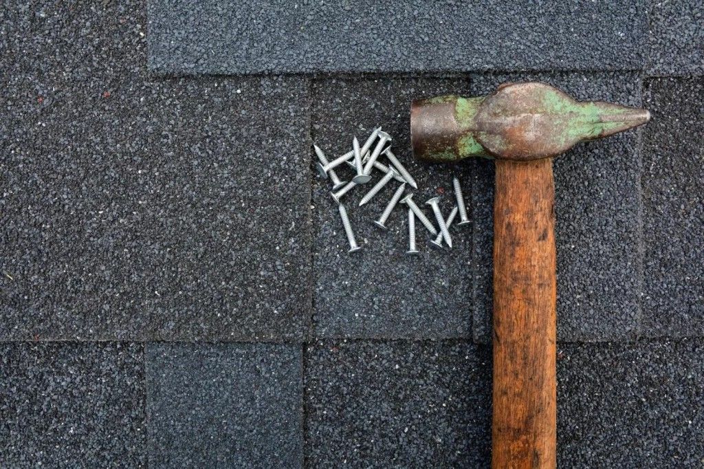 Hammer and nails on a dark-colored, textured roofing shingle. Hammer and nails on a dark-colored, textured roofing shingle.