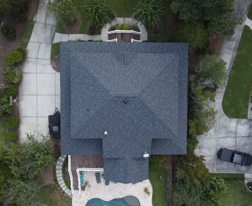 Aerial view of a dark gray roof with a pool and driveway. Trees and a car are visible in the surroundings.
