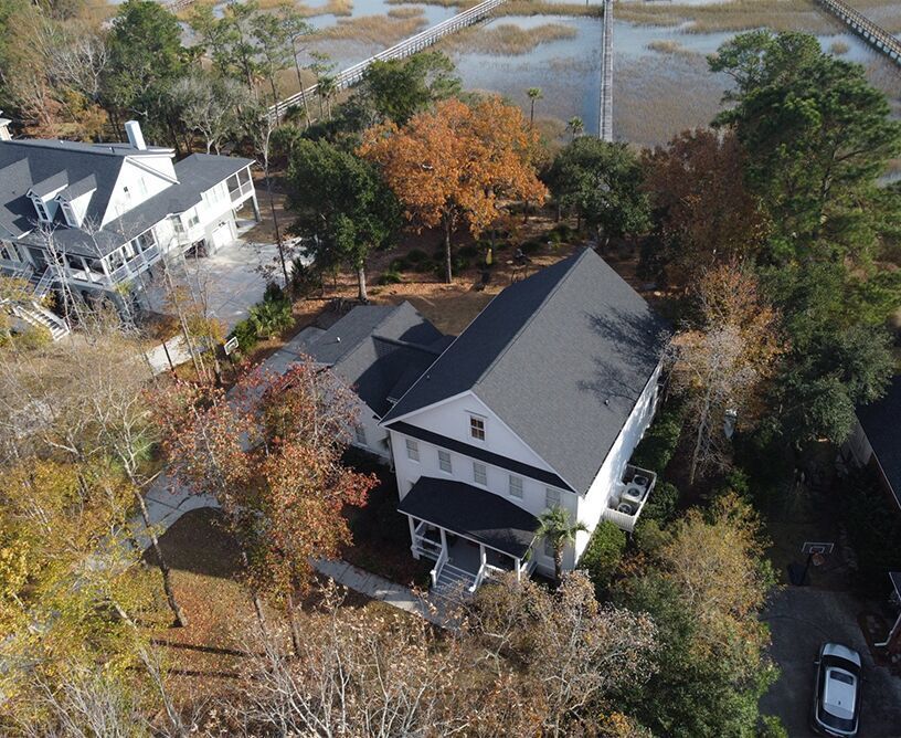Aerial view of a white house with a black roof, surrounded by trees with fall foliage, near water and docks.