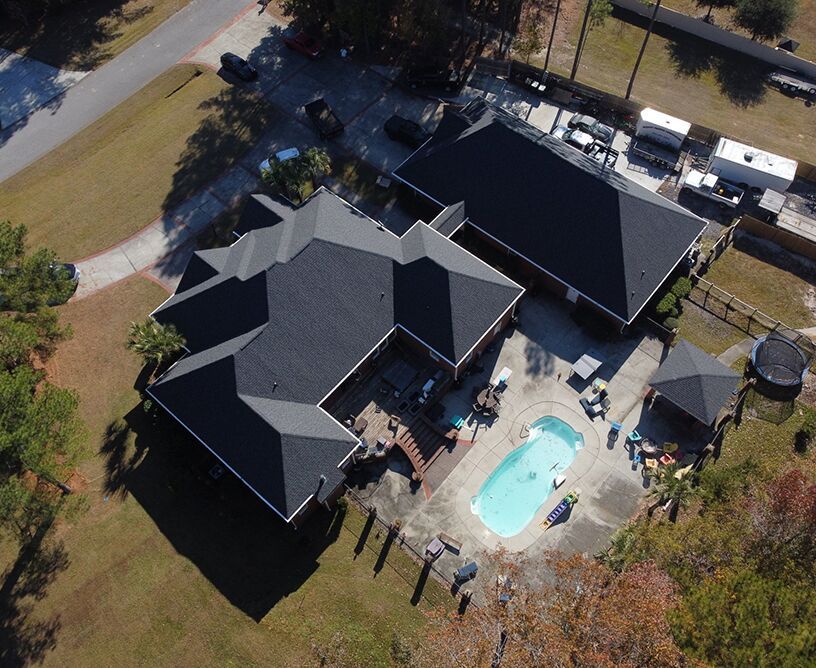 Aerial view of a house roof under repair, with new shingles in place; tarps cover objects below.