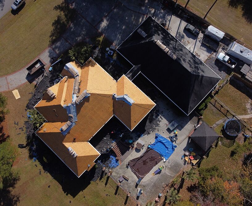 Aerial view of a house with a partially replaced tan roof, black roof, and debris around a pool.