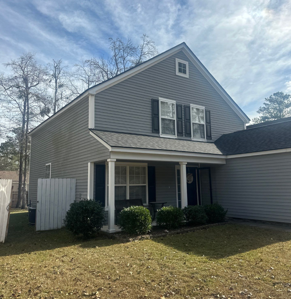 Two-story gray house with a porch and bushes in front on a cloudy day.