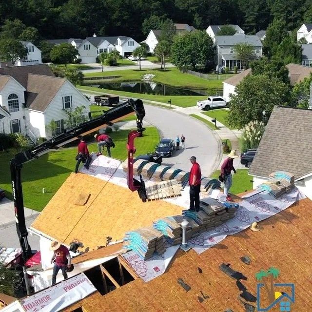 Roofers installing shingles on a house roof with a crane in a residential neighborhood. Roofers installing shingles on a house roof with a crane in a residential neighborhood.
