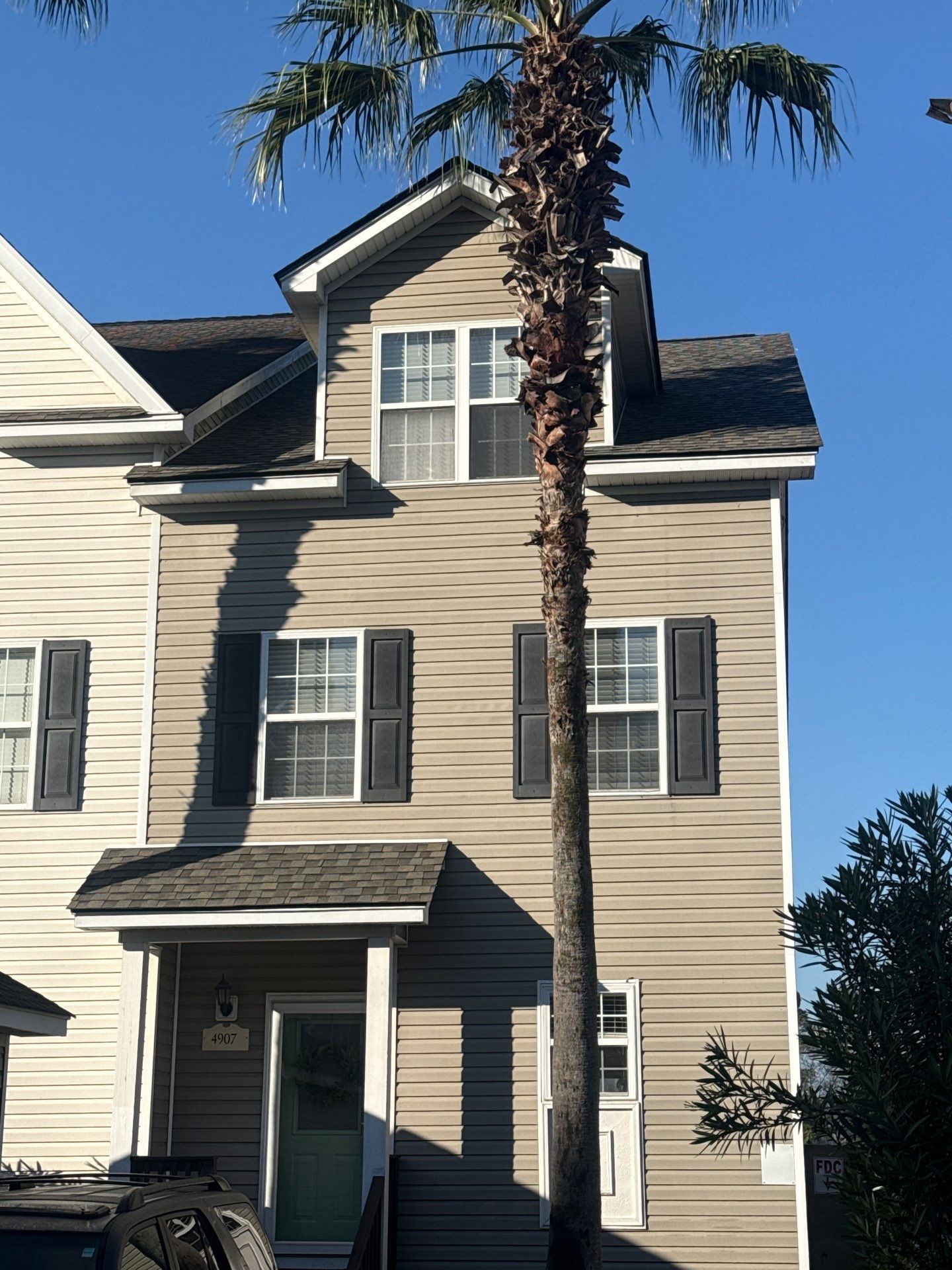 Tan three-story house with dark shutters, under a palm tree against a clear blue sky.