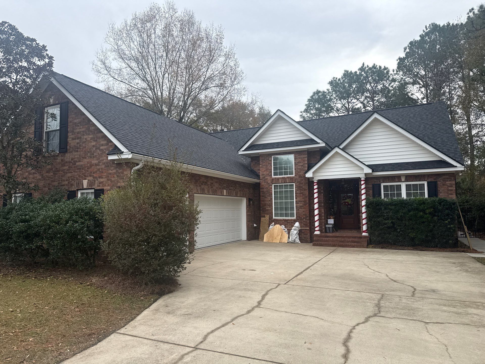 Brick house with dark roof and white trim, front yard, concrete driveway, overcast sky.