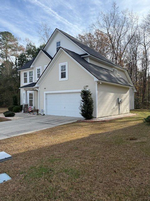 Two-story house with a white garage door, light siding, and a driveway on a grassy lawn.