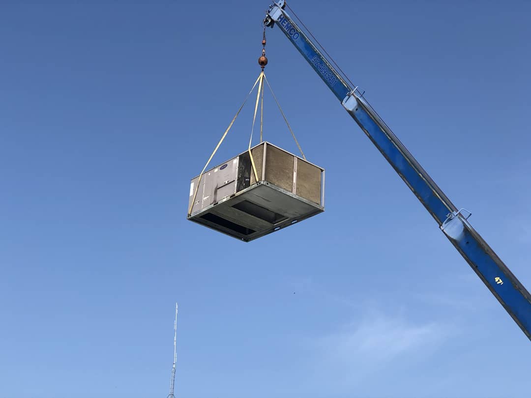 a crane is lifting a large commercial ac unit in the air .