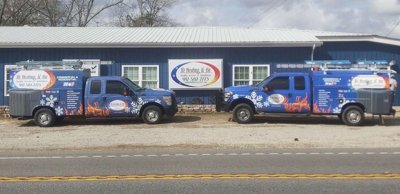 two JD Heating & Air trucks are parked in front of the JD heating and air building .