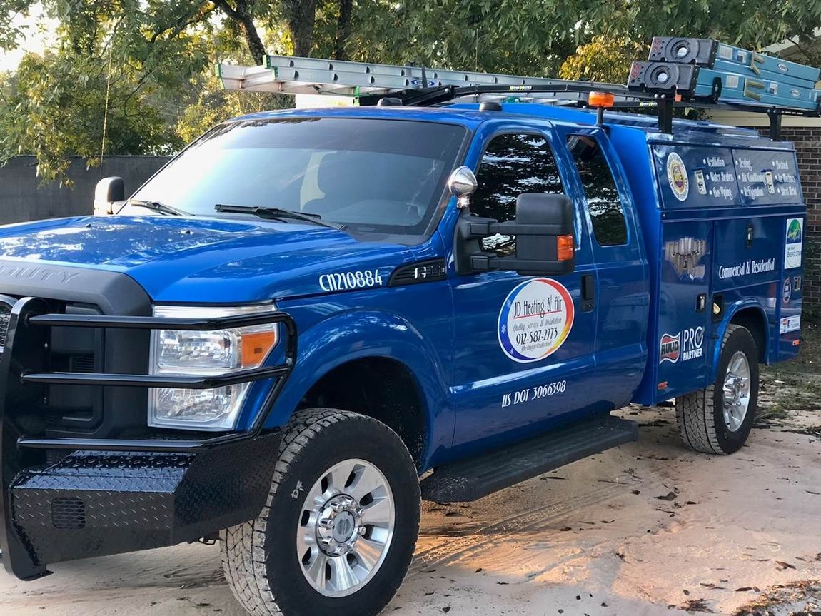 a blue jd heating & air truck with a ladder on top of it is parked in a driveway.
