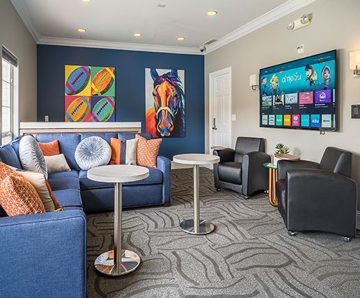Living room with blue couch, horse art, TV, armchairs, and round tables.