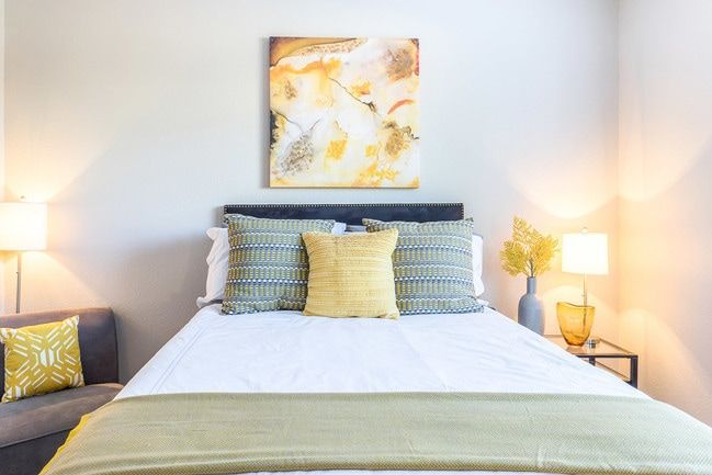 Bedroom with bed, pillows, artwork, lamps, and gray accent chair.