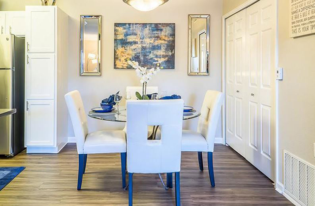 Dining room with a glass-top table, four white chairs, and abstract art on the wall.
