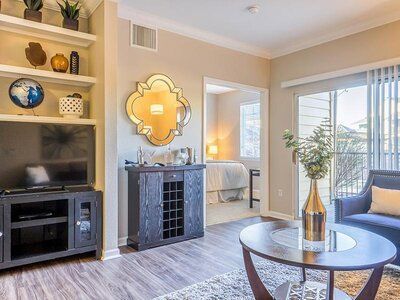 Living room with TV, bar, mirror, and sliding glass door to balcony, beige walls, hardwood floors.