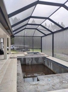 Screened-in pool area with a hot tub and stone patio beside a house