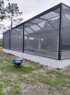 Mesh-covered outdoor enclosure with black frame and white base on a grassy dirt lot