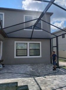 Screened patio under construction beside a gray house, with a worker standing at the right.