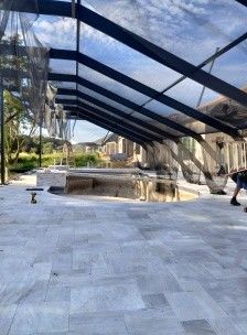 Outdoor patio with a large black mesh canopy and a stone walkway beside a pool or pond waterfall.