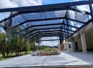 Covered outdoor walkway with black canopy beams and a paved courtyard beside a white building
