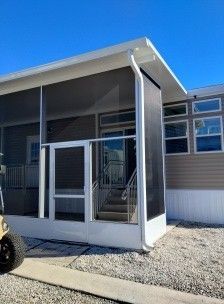 Covered porch entrance with white railings and stairs on a beige mobile home under a blue sky