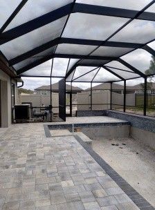 Covered backyard patio with pavers, screened enclosure, and an in-ground pool area under construction