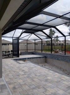 Backyard patio with screened pool enclosure and empty hot tub area on a stone paver deck