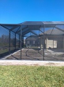 Black mesh outdoor enclosure beside a house, with blue sky and grass in front.