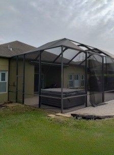 Screened porch with dark frame beside a house, overlooking a grassy yard