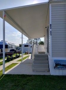 Mobile home entrance with white awning, steps, and small porch beside a parked RV.