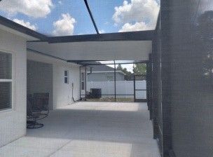 Covered patio walkway with concrete floor, black beams, and chairs beside a white building