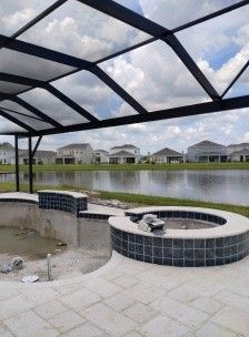 Covered patio with circular fire pit beside a pond, overlooking houses across the water.