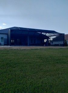Large metal warehouse with a dark roof beside a grassy field under a clear sky