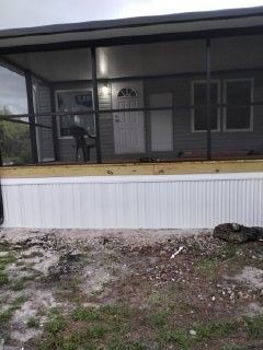 Screened porch with white double doors, a chair, and a person standing inside above a dirt yard.