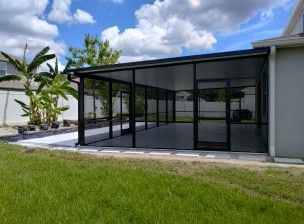 Screened patio enclosure beside a house, with black framing and glass panels overlooking a grassy yard.