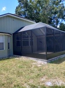 Screened-in porch attached to a light-colored house in a grassy yard.