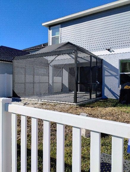Mesh patio enclosure beside a white house, viewed over a white fence on a sunny day