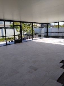 Spacious screened patio with gray tile floor, black framing, and bright sunlight from large windows.