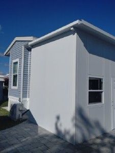 White house exterior with gray siding and a small window under a blue sky