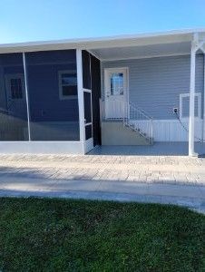 Covered front porch with screened left side, white door, and gray siding beside a paved walkway.
