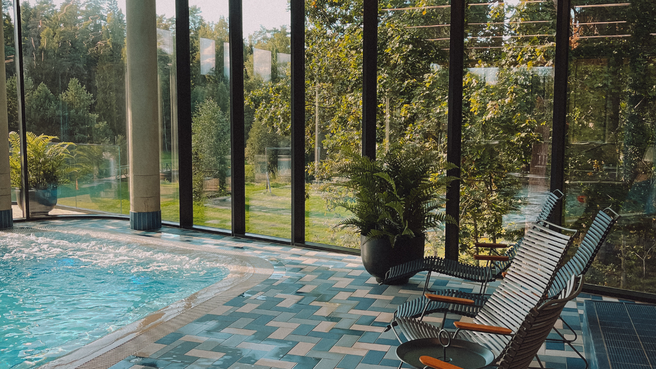 Indoor pool with lounge chairs by tall windows overlooking a leafy garden