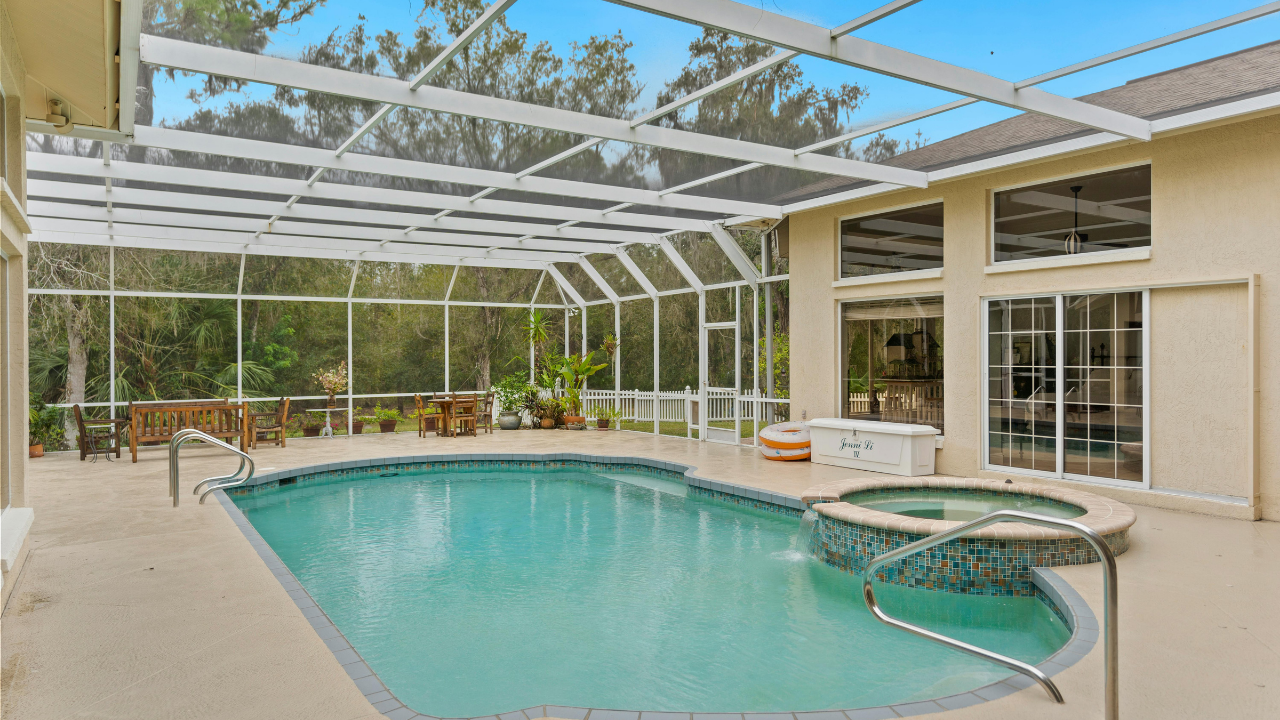 Screened-in backyard pool with turquoise water, beige patio, and white patio furniture under a covered lanai