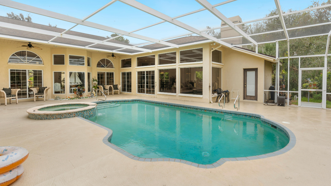 Screened-in backyard pool with beige deck and lounge chairs under a white patio enclosure