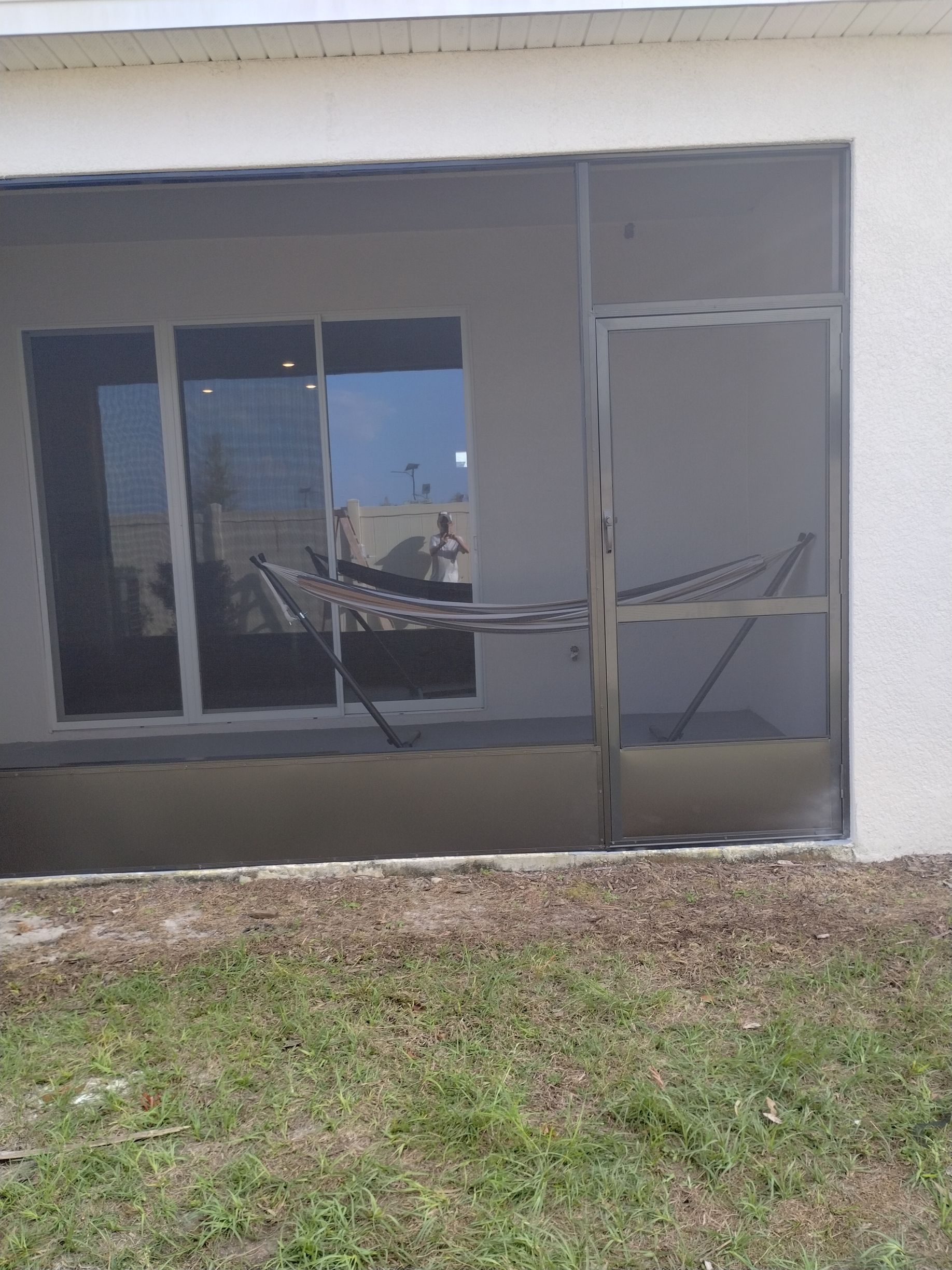 Covered patio with a sliding glass door and hammock, next to a grassy yard.