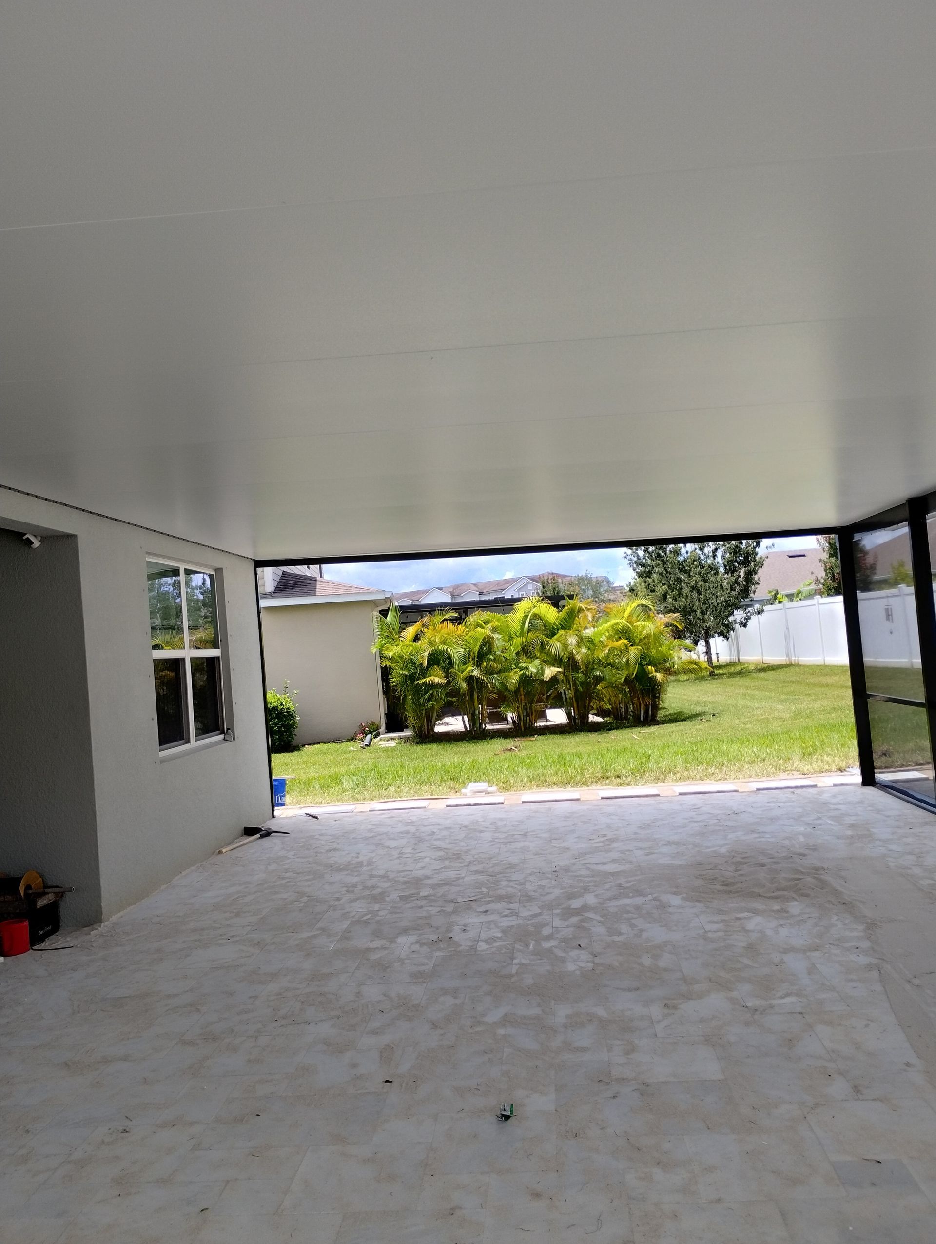 Covered patio opening to a sunny yard with green lawn and shrubs