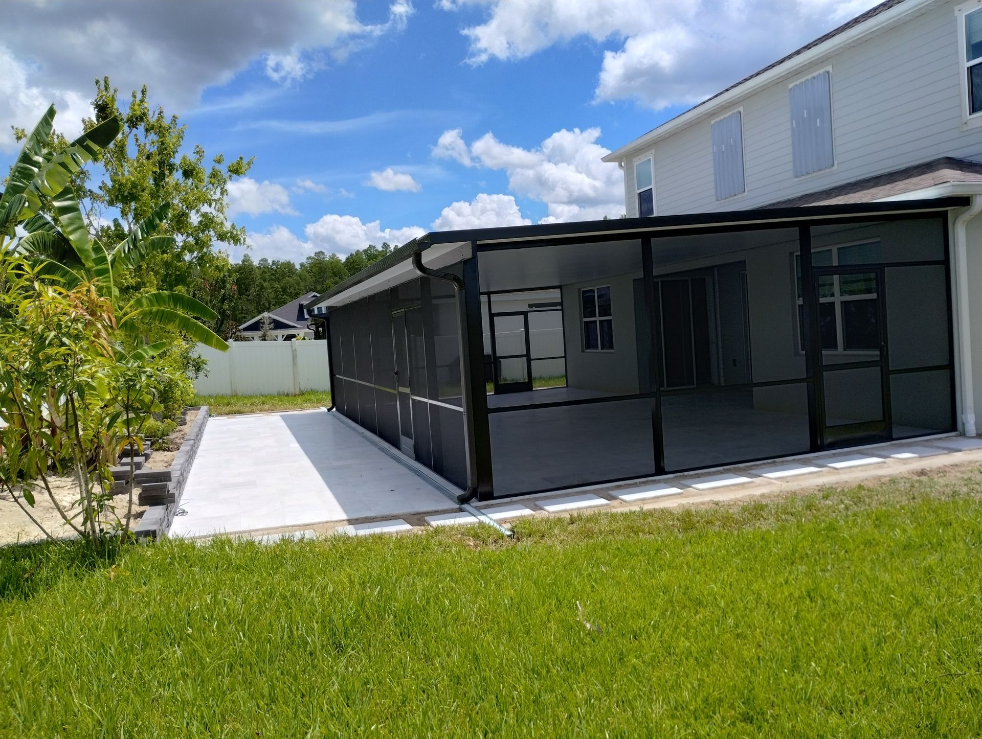 Screened patio attached to a two-story house with a concrete walkway and grassy yard under a blue sky