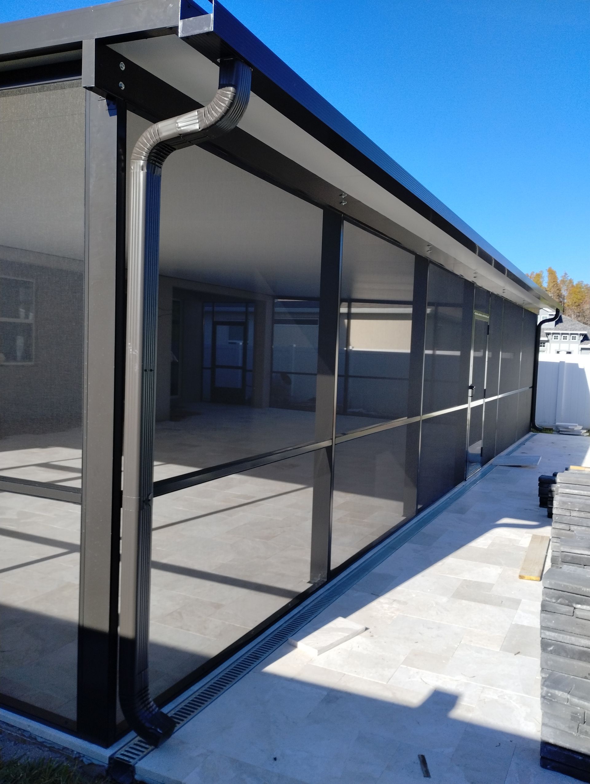 Black screened patio enclosure attached to a gray house, with a snowy walkway beside it.