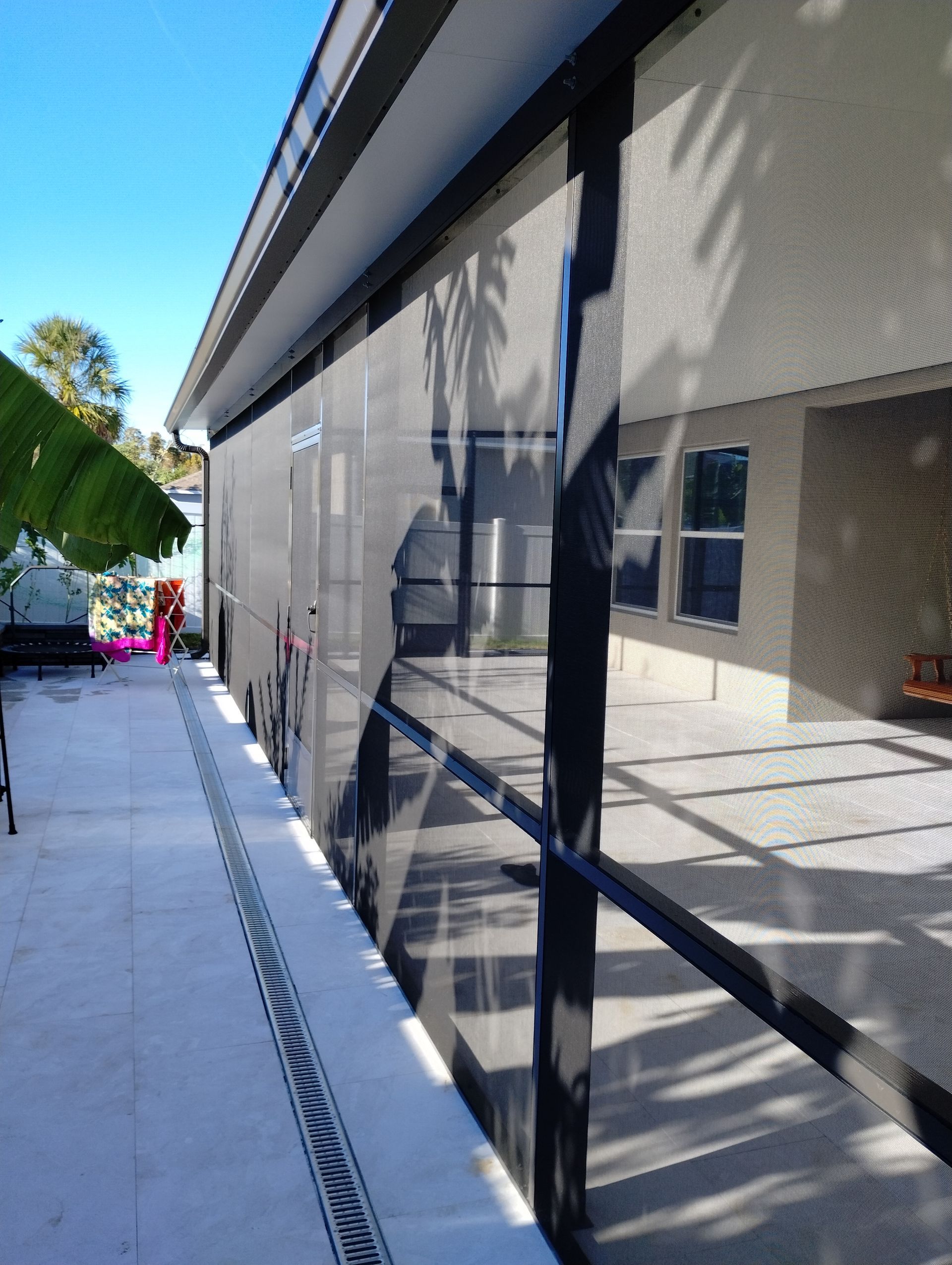 Narrow side walkway beside a modern building with mesh-covered windows and a drainage channel.