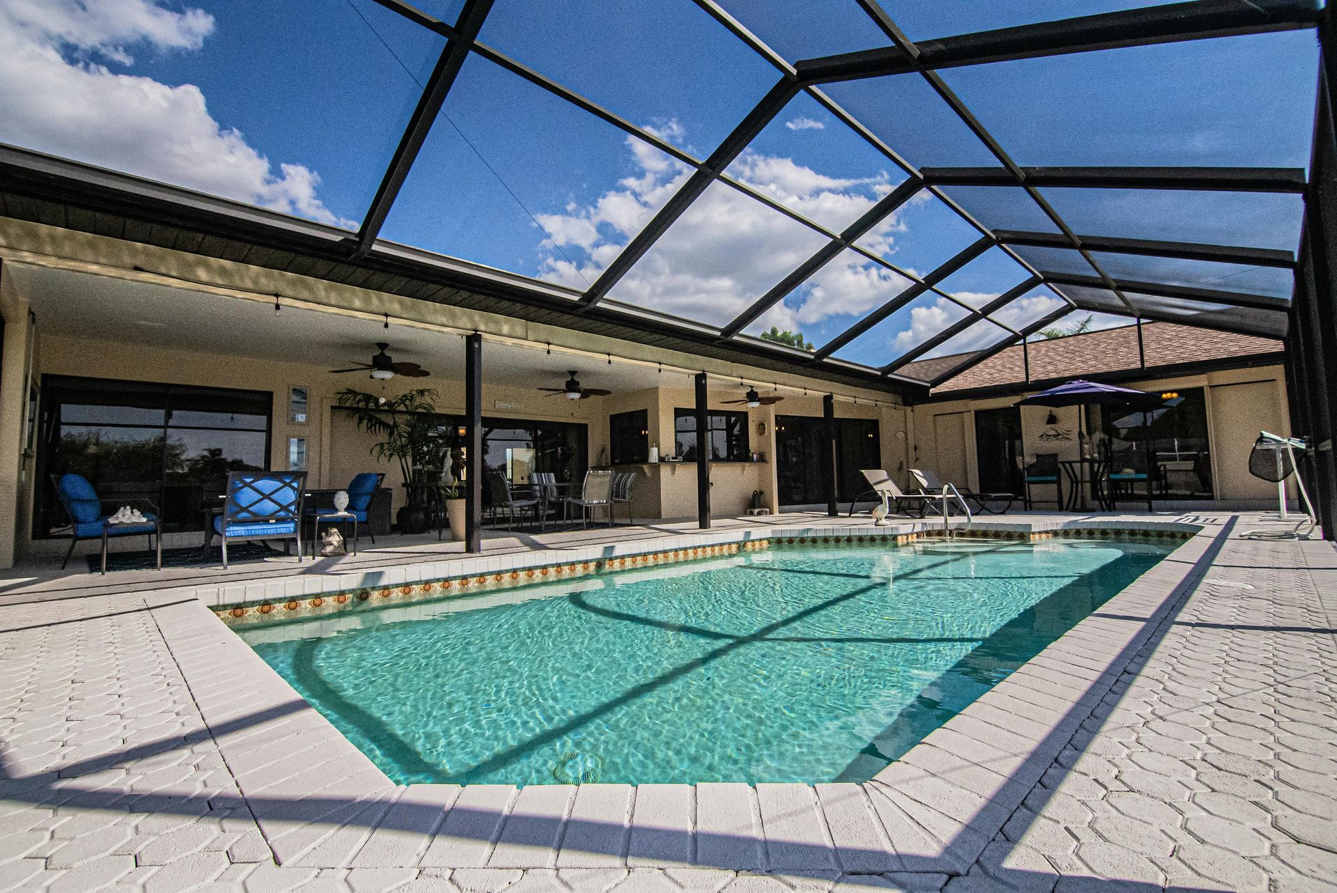 Screened-in backyard pool with turquoise water, lounge chairs, and a patio under a blue sky