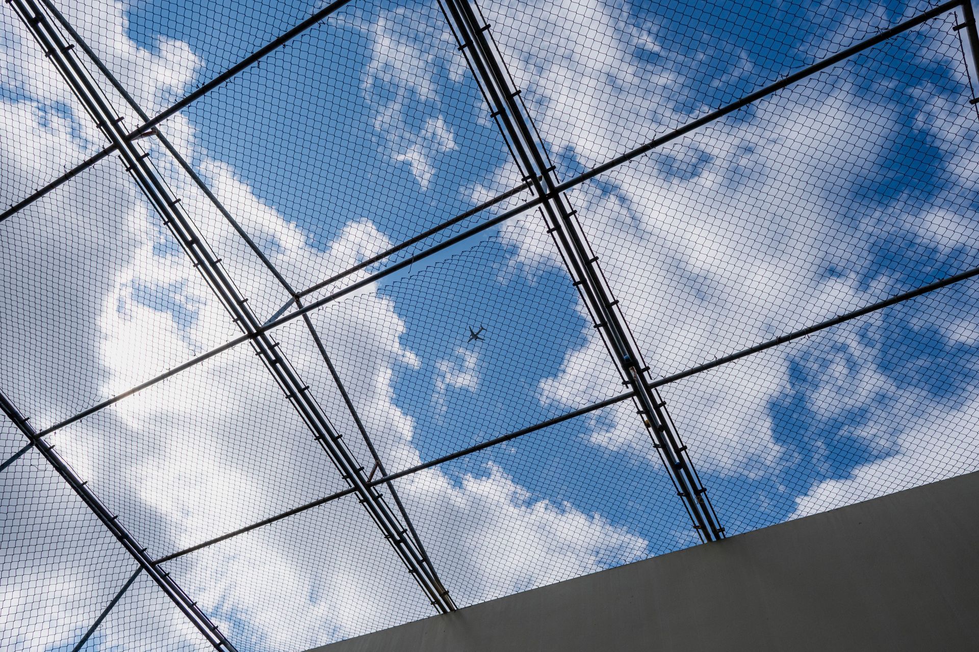 Netting overhead against a blue sky with scattered clouds and a building edge below