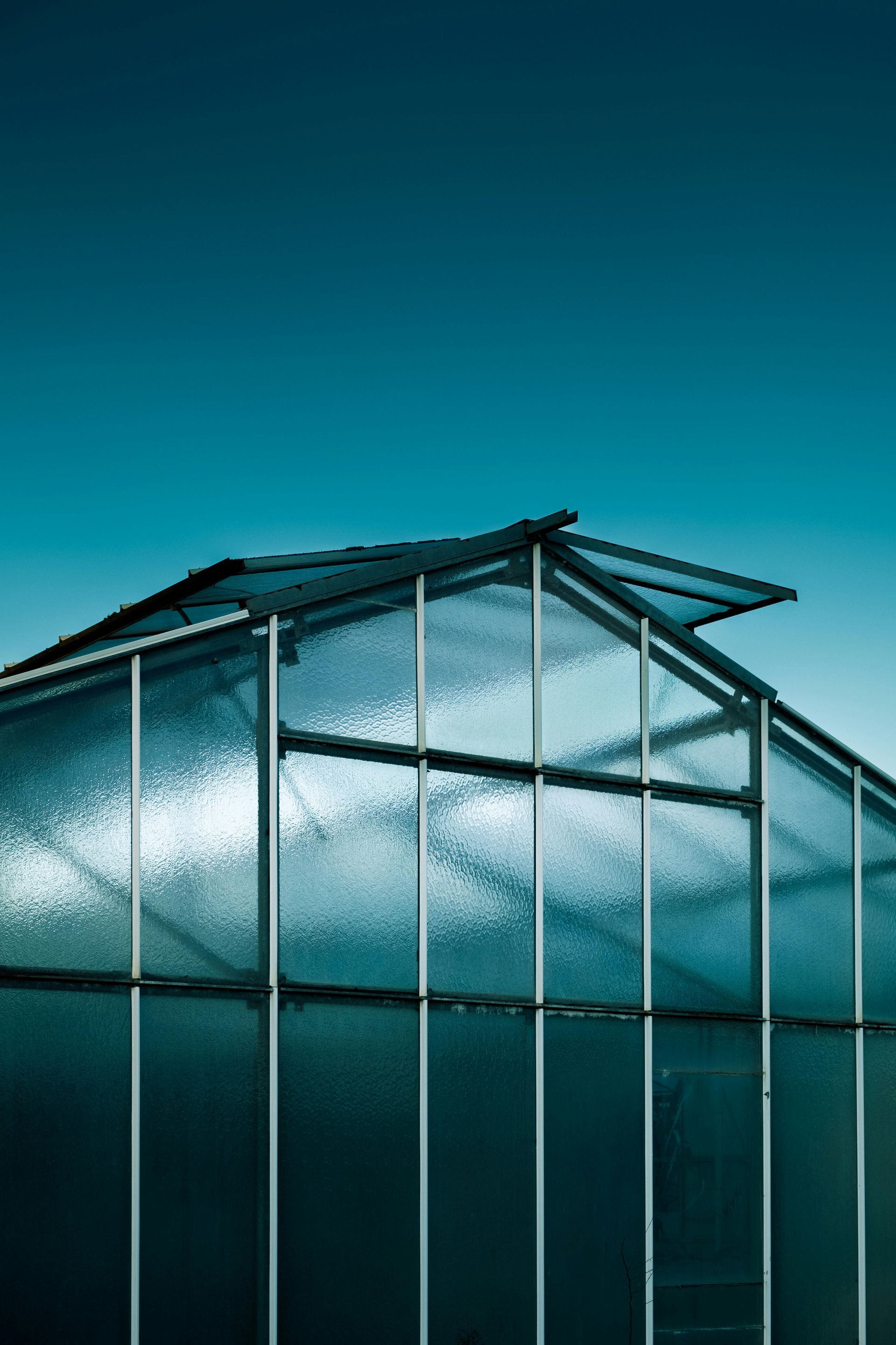 Glass greenhouse with a blue roof against a teal sky